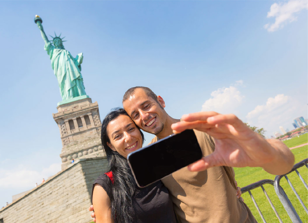 tourist couple taking a selfie in front of statue of liberty